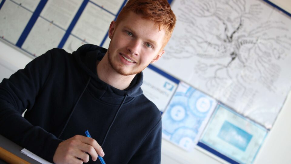 Student sitting at a desk holding a pen and smiling