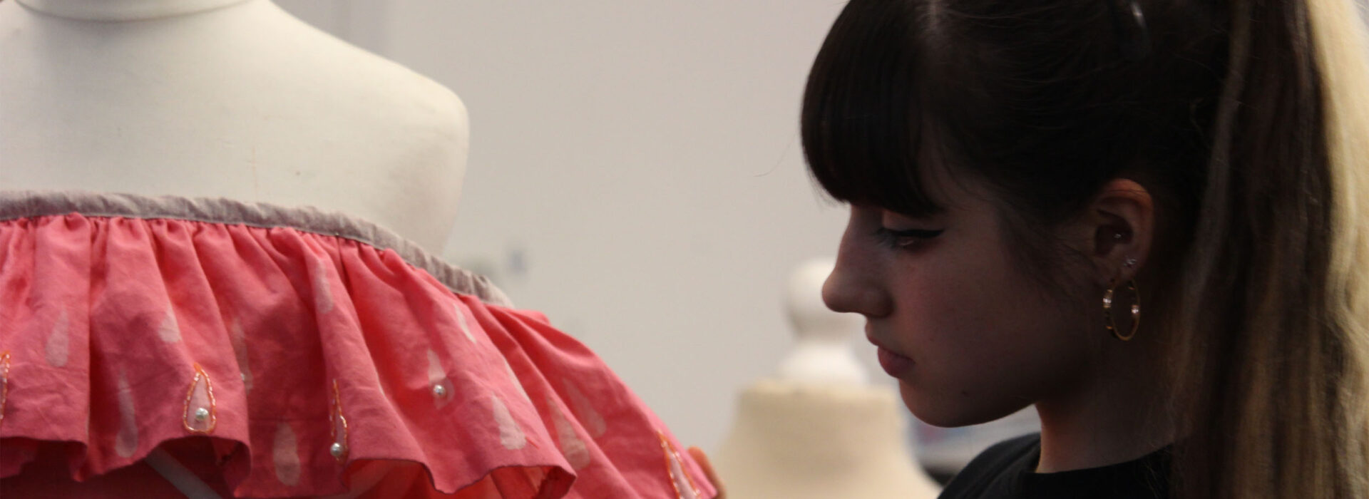 Photograph of a textiles student standing next to a dress she has made.